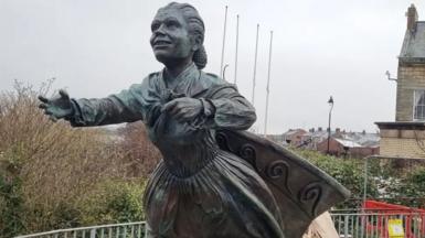 A sculpture depicts a woman stretching out her arms.  