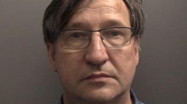 Police custody picture of Vladimir Motin. He has short dark hair with a parting and is wearing glasses. He is staring into the camera against a grey wall.
