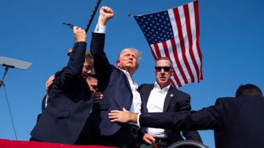 Donald Trump with blood on his face, surrounded by staff in front of an American flag
