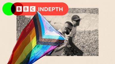 A black and white treated image of two men holding a rainbow flag
