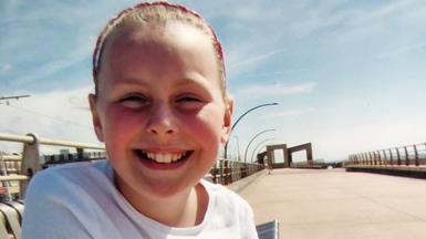 A young girl with a white top sits at a beach promenade