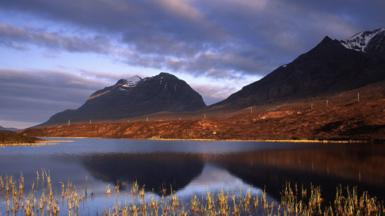 Loch le dà bheinn air a chùlaibh. Tha an adhar sgòthach.