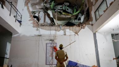 An official looks up with his arms behind his back and back turned to the camera, as they inspect a huge hole in the wall of a building interior, with some of the plane visible in the hole, on Thursday.