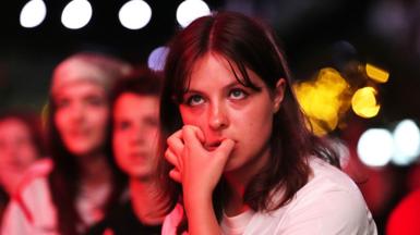 A young woman with shoulder length brown hair and a fringe bites her nails in Boxpark Croydon during the semi-final between England and Italy 