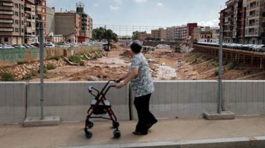 A woman walks on a bridge overlooking a riverbed full of mud