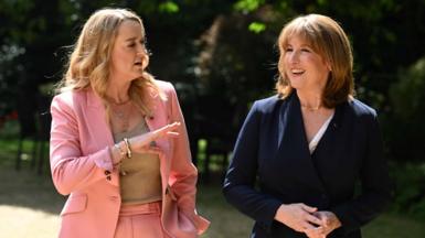 Laura Kuenssberg in pink on the left raises her right hand as she interviews Rachel Reeves on the right, in a blue suit, in a garden