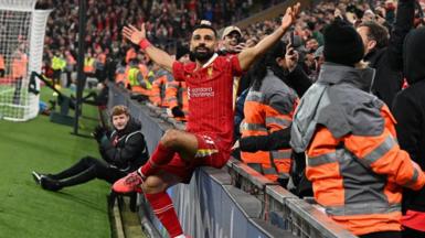 Mohamed Salah sits on an advertising board as he celebrates his goal against Aston Villa