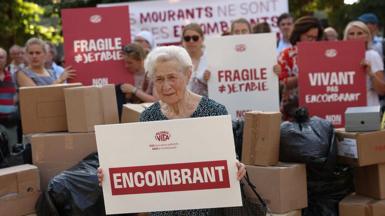 A protester sits with a placard that reads "Burden" during a rally organised by French "pro-life" organisation Alliance Vita against the new French draft law on euthanasia and assisted suicide at Invalides, in Paris on June 22, 2026