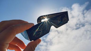 A pair of eclipse glasses held up in front of the sun