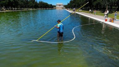 Workers with long poles clean the pool with the Lincoln Monument in the background