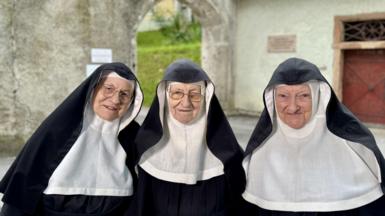 Three nuns stand in front of the monastery in their habits, with Sister Rita on the left and Sister Regina in the centre both wearing glasses