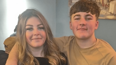 The picture shows two people smiling at the camera. The girl on the left has brown, long hair, and the boy on the right has short brown hair. 