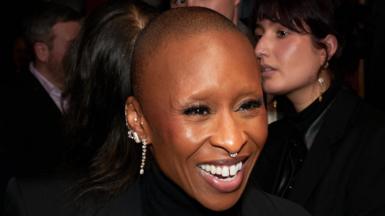 Cynthia Erivo smiling at a Wicked: For Good event, she is wearing several diamond earrings and a diamond nose ring. Her head is shaved.