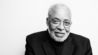 A black and white portrait of James Earl Jones, who is wearing glasses, a black polo neck jumper and a black blazer on top