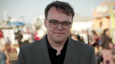 Pavel Talankin looking direct to camera in a grey suit and black top, with people behind him