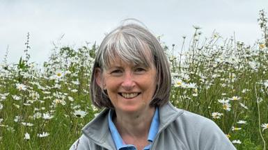 Woman with grey hair and fringe sitting in a field of daisies 