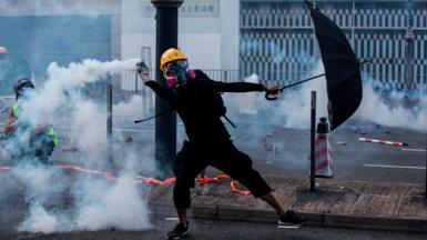 A protester fully clad in black, and wearing a respirator mask and a yellow helmet,  throws a tear gas canister fired by police in the Sha Tin district of Hong Kong on October 1, 2019, as the city observes the National Day holiday to mark the 70th anniversary of communist China's founding. 