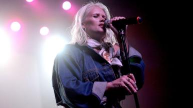 Lauren Bennett sings onstage during a concert. She wears a denim jacket