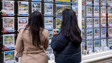 Two women with long dark hair look in an estate agent's window