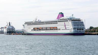 A large cruise ship, which is white, with purple and green markings, is seen docked at a port 