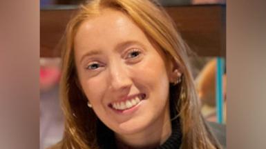 Close up of Chloe Moffat, who has long red hair, smiling at a camera.