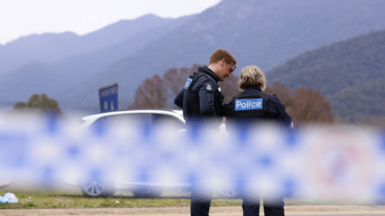 Two police officers stand behind police tape in Porepunkah, green mountains can be seen in the background