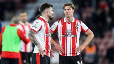 Two Southampton players, wearing red and white striped shirts and black shorts, in conversation