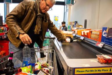 A man loading a trolley of shopping onto a till conveyor belt at Lidl