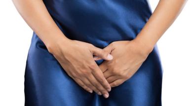 A anonymous woman stands with her hands shielding her pubic area