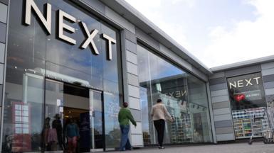 A Next store is seen with the logo looming large over passers-by as they walk outside the storefront on a sunny-cloudy day in Basildon in October.