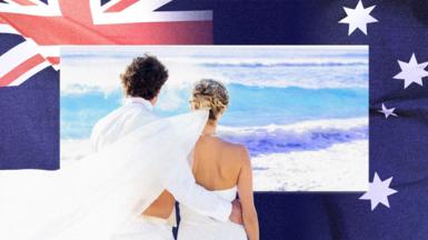 A newlywed couple are seen looking out to sea on a beach, with a photo of the Australian flag in the background. 