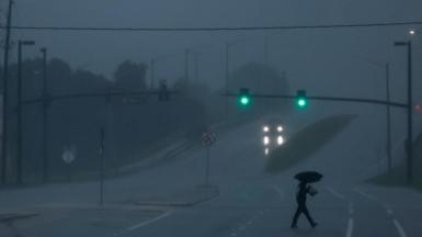 A man with an umbrella crosses a road as Hurricane Milton approaches, in Orlando, Florida