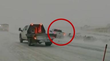 A vehicle circled in red nearly collides with a person on the side of a white snow-covered road as another service truck drives nearby in the foreground.