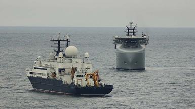 Russian ship Yantar in the  foreground being watched by a Royal Navy ship close by 