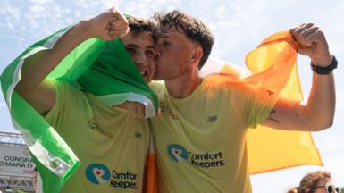 The brothers embrace one another at the end of their Ireland running challenge. Both of them have an Irish flag draped over their shoulders and Jordan kisses Cian on the cheek.
