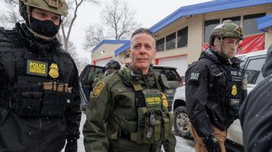 Gregory Bovino walks on a street flanked by two US Customs and Border Protection officers.