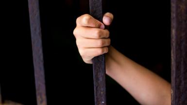 A child's hand gripping a jail bar