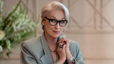 Image of Meryl Streep in a still from The Devil Wears Prada 2. She is wearing a grey blazer, assorted jewellery and black glasses.