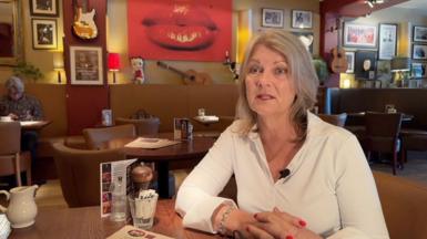 Amanda Brighton is sitting in a restaurant. She is wearing a white top.