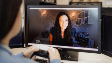 A young woman playing a video game on a screen in front of her holds a video game controller.