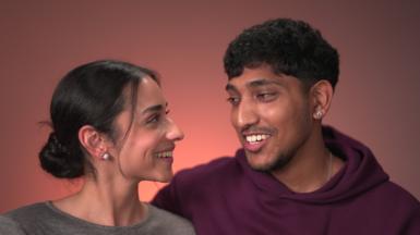 Nav Sangha and Adarsh Ramchurn smile as they look at each other. She is wearing a grey shirt and he is wearing a purple hoodie.