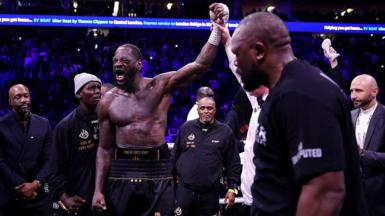 Deontay Wilder has his hand raised while Derek Chisora looks on