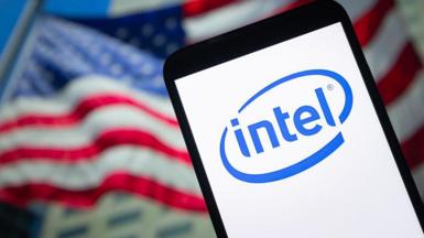 A mobile device displaying the Intel logo appears in front of a blurry US flag