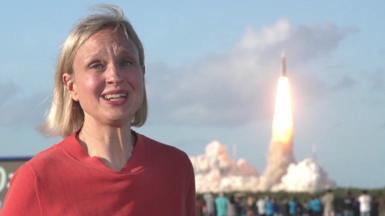 Rebecca Morelle in Florida, she has an excited expression as a rocket launches behind her