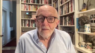 BBC International editor Jeremy Bowen wearing pale blue shirt and sitting in front of bookshelf