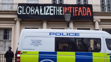 A police van is parked outside the Diorama building in London with a police officer standing next to it, and above the van is a banner reading 'Globalize the intifada' hung on the building, in 2023.