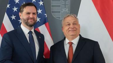 JD Vance and Orban stand together smiling, in front of their national flags
