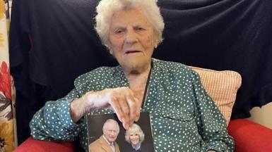 Ethel Caterham sat holding a card with a picture of the King and Queen on the cover.