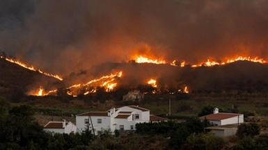 Flames tear through the hills around houses. 