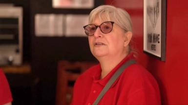A woman wearing a red top answers questions inside a shop